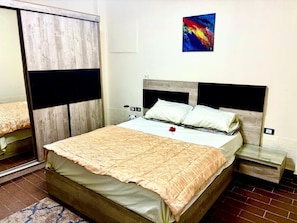 Une chambre à coucher avec un lit, une table de chevet, un miroir et un tableau abstrait aux couleurs vives accroché au mur.