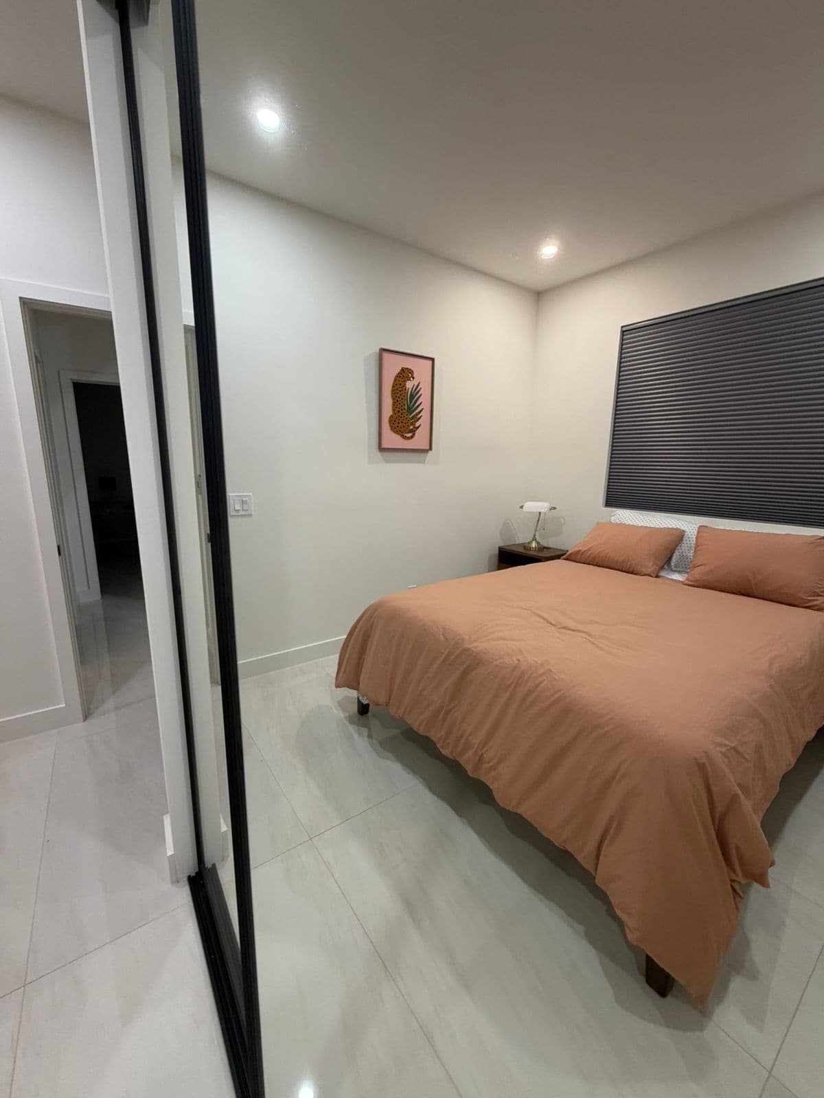 A bedroom with a bed, a nightstand, a lamp, a picture on the wall, and a door leading to another room.