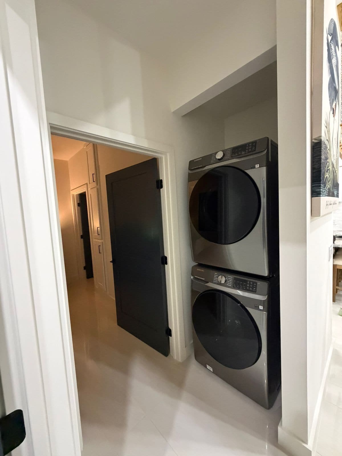 A laundry room with two stacked front-loading washers and dryers, a white door leading to a hallway, and a tiled floor.