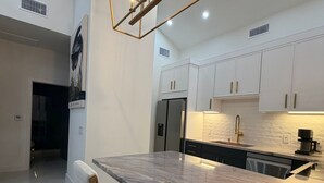Une cuisine moderne dotée d’un plan de travail en marbre, de tabourets de bar en bois et de luminaires suspendus.