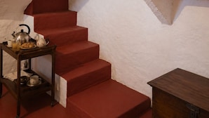 A staircase with red steps leading to a white wall, a small table with a kettle and teapot, and a shelf with a pot. - Quinta Farm stay (Lousã)