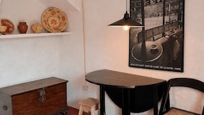A room with a wooden cabinet, a small stool, a round table, a black chair, a woven rug, and a poster on the wall. - Quinta Farm stay (Lousã)