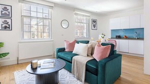 Een moderne woonkamer met een turquoise bank, een ronde salontafel en een keuken met witte kasten en een blauw aanrecht.