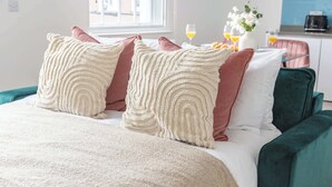 Een bed met decoratieve kussens, een bekleden hoofdbord in groen en een raam met uitzicht op gebouwen.