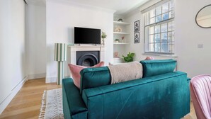 Een smaragdgroene bank met een flatscreen-tv, een open haard, een raam en een spiegel aan de muur.