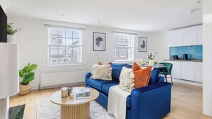 Una sala de estar moderna con un sofá azul, una mesa de centro redonda y vistas de la ciudad a través de grandes ventanales.