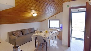 A room with a wooden ceiling, a sofa, a dining table with chairs, a TV, and a door leading outside. - Relaxing Retreat With Terrace (Umag)