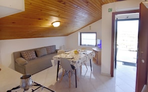 Ein Zimmer mit Holzboden, einer Couch, einem Esstisch mit Stühlen, einem Fernseher und einer Tür, die nach draußen führt.