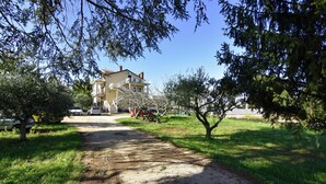 A pathway leading to a building with a balcony, surrounded by trees and parked cars. - Relaxing Retreat With Terrace (Umag)