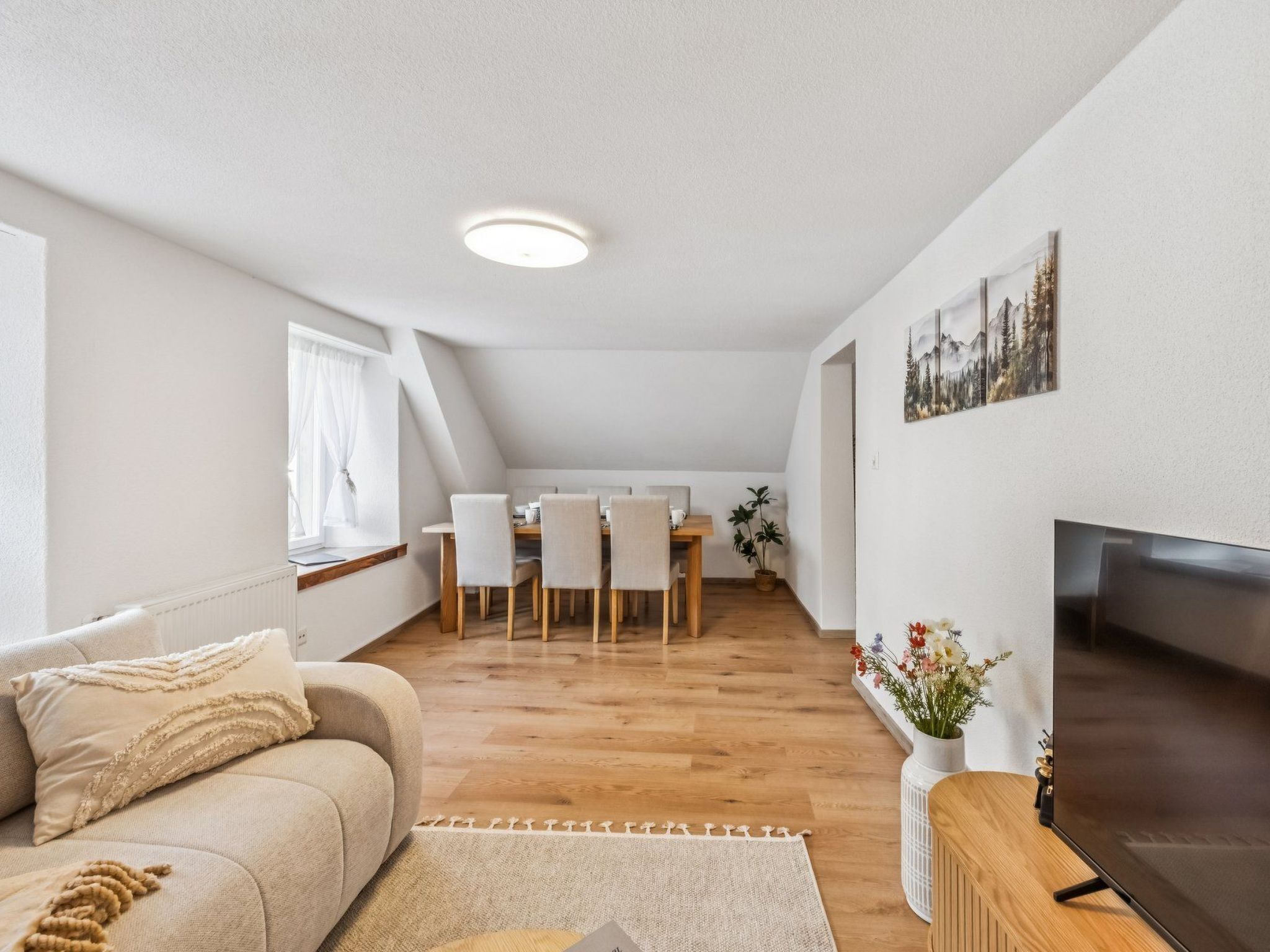 Ein modernes Wohnzimmer mit einer Couch, einem Fernseher und einem Essbereich mit Stühlen und einem Tisch.