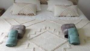 Una cama con un cabecero estampado, dos almohadas con diseño en zigzag y dos toallas enrolladas.