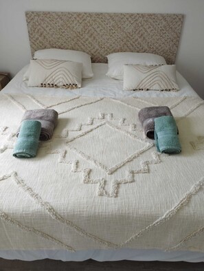 Ein Bett mit einem gemusterten Kopfteil, zwei Kissen mit Zickzackmuster und zwei aufgerollte Handtücher.