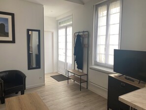 Ein Zimmer mit Holzboden, einem schwarzen Ledersessel, einem Fernseher auf einem Holztisch, einem Kleiderständer mit einer Jacke und einer Tür zu einem anderen Raum.