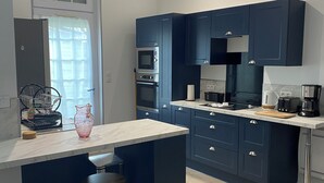 Una cocina moderna con armarios azul oscuro, encimera de mármol y horno integrado. Hay dos taburetes en la isla y una ventana con cortina.