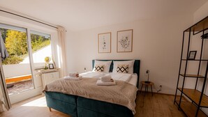 A bedroom with a bed, a bedside table, a radiator, and a window. - Come4Stay Passau - 2 Zimmer - bis zu 4 Gäste by Interhome (Passau)