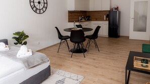 A modern hotel room with a bed, a dining table with chairs, a kitchen area, and a large wall clock. - Come4Stay Passau - 2 Zimmer - bis zu 4 Gäste by Interhome (Passau)