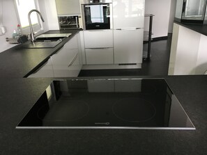 Eine moderne Küche mit einem schwarzen Induktionskochfeld, einem eingebauten Backofen und einer Mikrowelle.