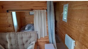 Et interiør af en træhytte med sofa, gardiner, en radiator og et lille vindue.