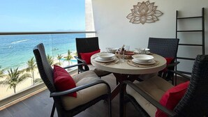 Ein Essbereich mit Tisch für vier Personen, mit Blick auf einen Strand mit Palmen und dem Meer.