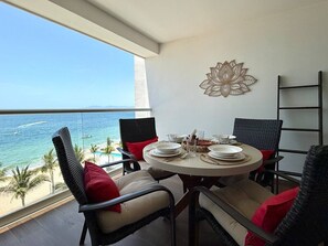 Ein Essbereich mit Tisch für vier Personen, mit Blick auf einen Strand mit Palmen und dem Meer.