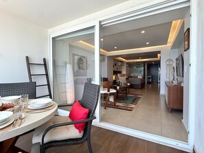 Ein Essbereich mit einem Tisch für zwei Personen, einem Stuhl mit rotem Kissen und einer Schiebetür zu einem Wohnzimmer mit Sofa und Couchtisch.