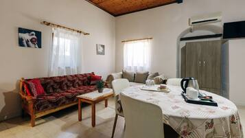 A living room with a sofa, a dining table with chairs, a coffee table, and an air conditioning unit.