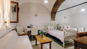 A room with two beds, a sofa, a wooden table, a chair, and a small table with a plant.