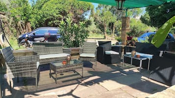 An outdoor patio area with wicker furniture, a glass table, and a stone floor.