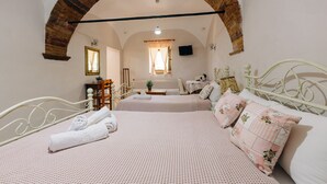 A room with two beds, a brick archway, a television, and a small table with a plant.