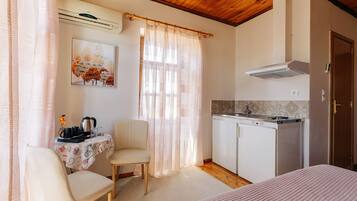 Una habitación con cama, una mesa de comedor con sillas, una kitchenette y una ventana con cortinas traslúcidas.