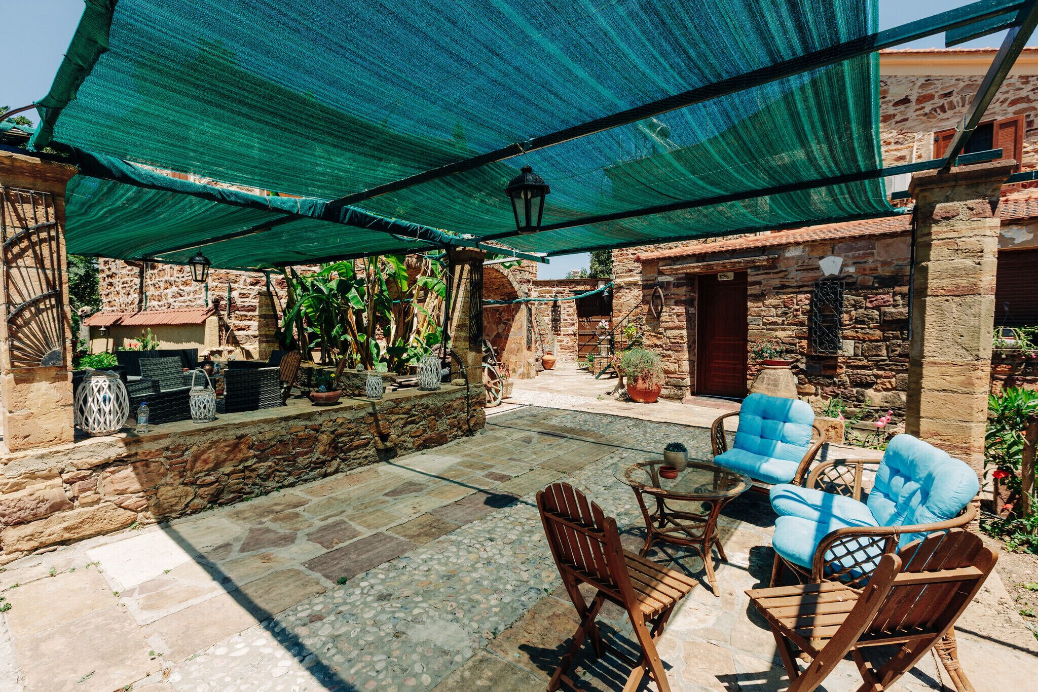 A patio with stone flooring, wooden furniture, and a green canopy.