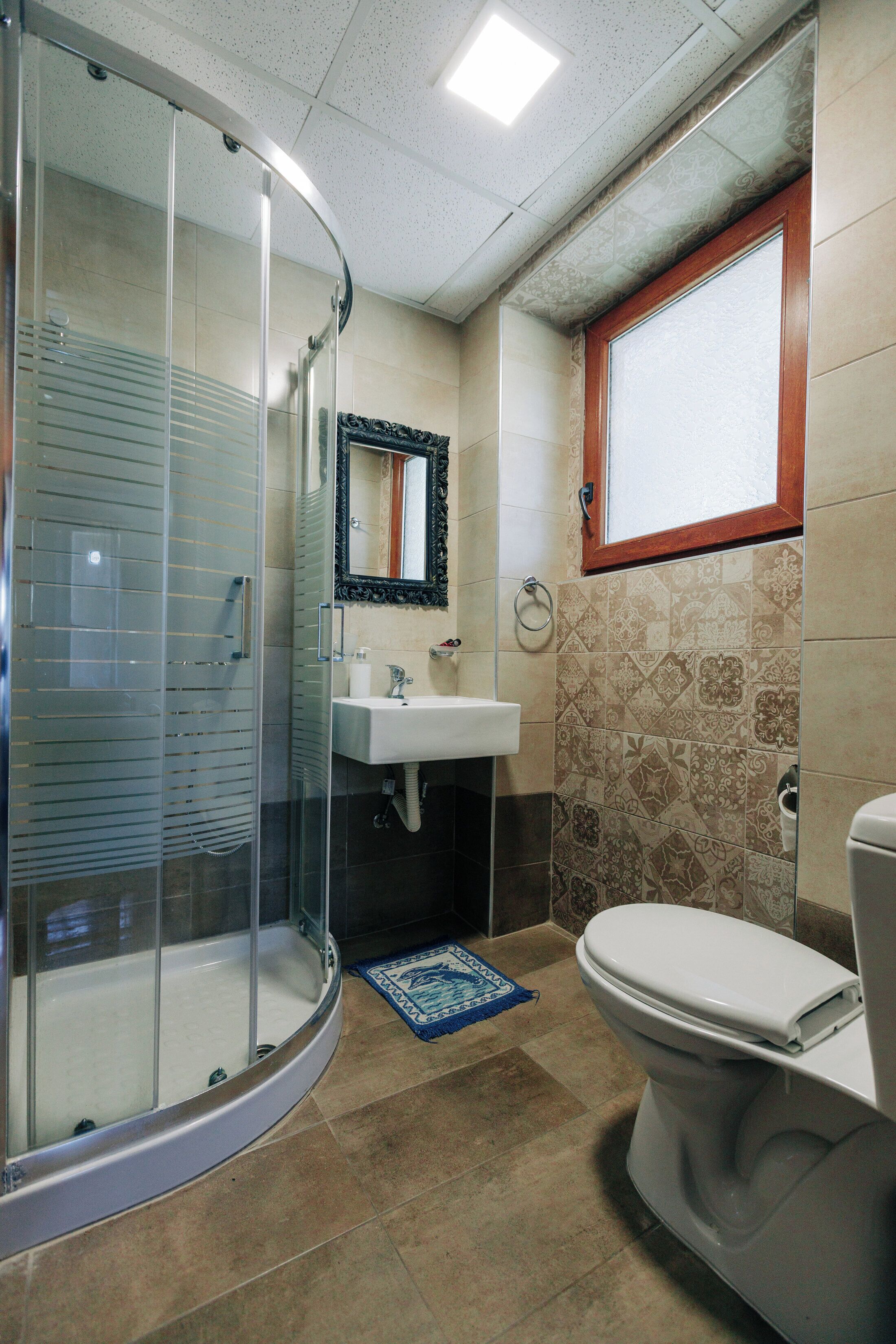 Un baño con ducha de vidrio, lavabo, inodoro y azulejos estampados.