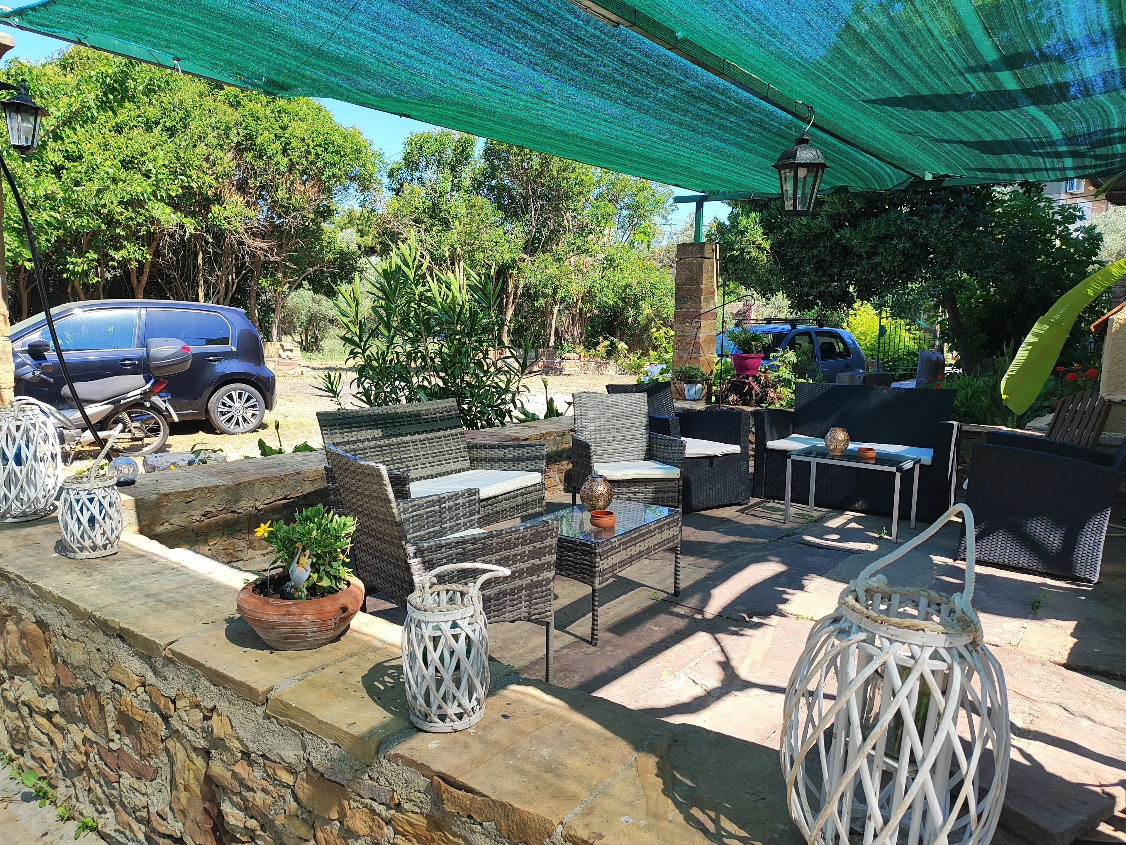 An outdoor patio with wicker furniture, stone walls, potted plants, and a green canopy.