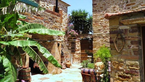 A narrow stone courtyard with a rustic building, a wooden barrel, and potted plants.
