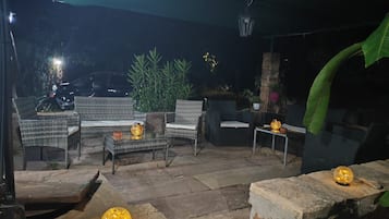 Een terras met rieten meubels, stenen tafels en decoratieve verlichting.