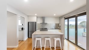 A modern kitchen with a central island, stainless steel appliances, and a sliding glass door to a balcony. - Sunsets & Slow Days - Rosebud Family Retreat (Rosebud)