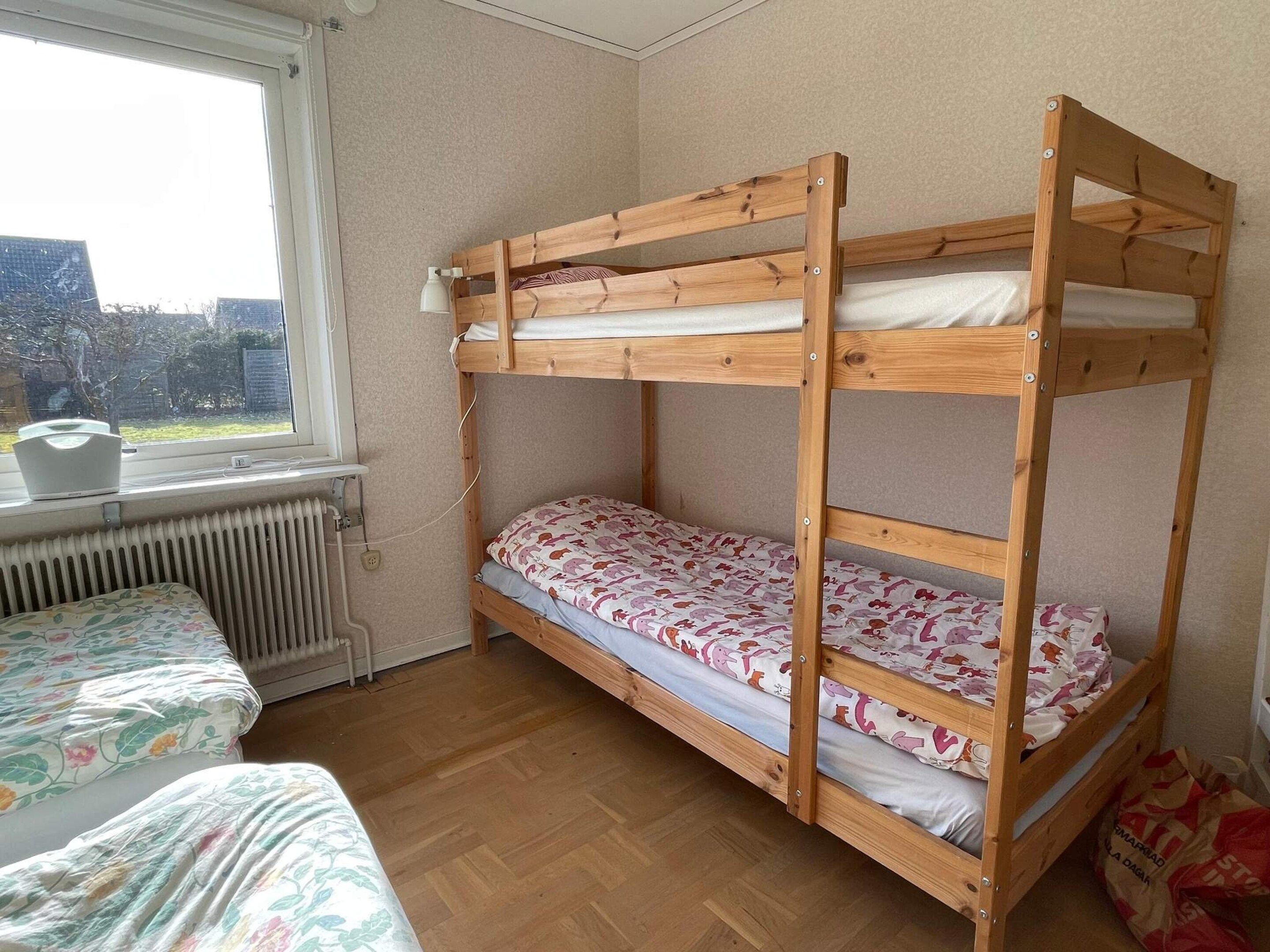 Uma cama beliche com janela, um radiador e uma cama com roupa de cama florida.