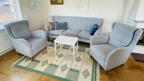 Ein Wohnzimmer mit grauem Sofa, zwei Sesseln, einem weißen Couchtisch und einem gemusterten Teppich.
