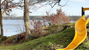 Ein Spielplatz mit Rutsche, Bäumen und einem Wasserspiegel im Hintergrund.