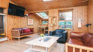 Ein gemütliches Blockhauskamin-Interieur mit Holzwänden, einem Essbereich, einer Couch, einem Couchtisch und einem an der Wand befestigten Fernseher.