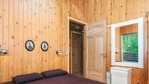 Ein Zimmer mit Holzwänden, einem Bett, einer Tür, einer Wandleuchte und einem Fenster mit Blick.