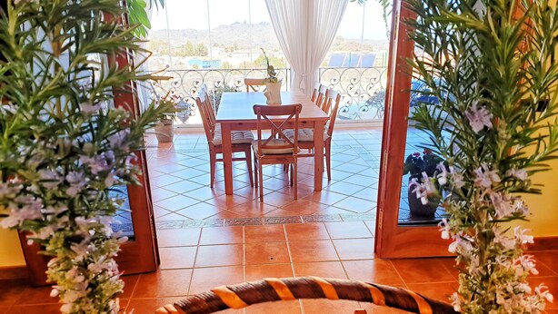 Zona pranzo con tavolo e sedie, vista all'esterno e un vassoio di frutta in primo piano.