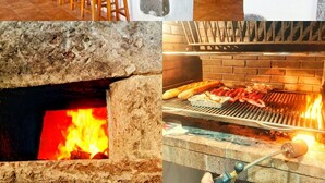 Una cucina con parete in pietra, un'area bar con sgabelli, forno a incasso e una griglia su cui si stanno preparando cibi.
