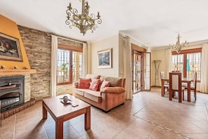 A living room with a fireplace, a sofa, a dining table, and a chandelier. - Villa Lorena with Pool, 4 bedrooms and parking (Nerja)