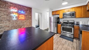 Een moderne keuken met houten kastjes, roestvrijstalen apparatuur en een neonbord aan de muur.