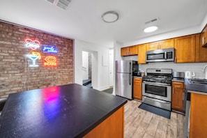 A modern kitchen with wooden cabinets, stainless steel appliances, and a neon sign on the wall. - Trendy and Comfortable Stay in Hyde Park (Chicago)