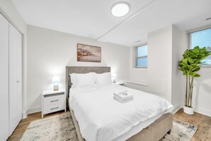 A modern bedroom with a bed, bedside tables, a nightstand, a window, and a potted plant. - Trendy and Comfortable Stay in Hyde Park (Chicago)