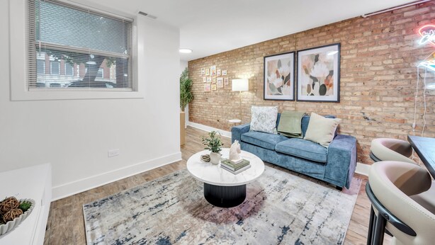 Een woonkamer met een blauwe bank, een ronde salontafel en een bakstenen muur met ingekaderde foto's.