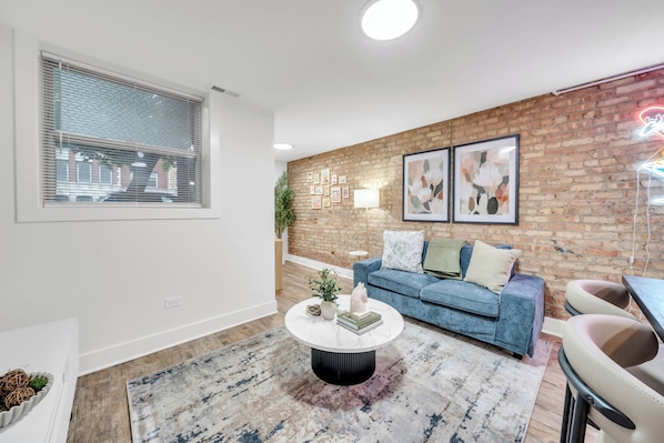 A living room with a blue sofa, a round coffee table, and a brick wall with framed pictures. - Trendy and Comfortable Stay in Hyde Park (Chicago)