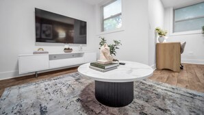 Een moderne woonkamer met een grote flatscreen televisie, een ronde salontafel, een witte dressoir en een houten vloer.